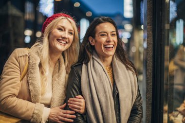 İki kadın bir dükkanı pencereden bakarak önden görünümü. İki kadın gülerek ve gülümseyerek mağaza içine bakarak dışarı durdu.