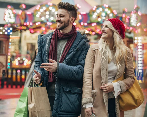 Waist up, front view of a couple walking on a city street with shopping bags in their hand.