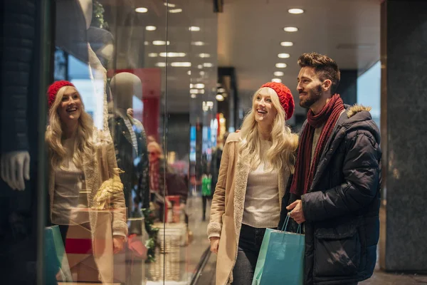 Front view of a couple walking past a shop window and looking in. They are shopping during the sales. The man is holding shopping bags.