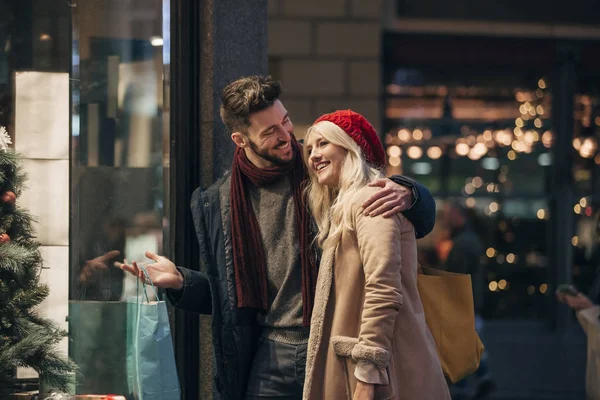 一对夫妇看通过商店窗口 而圣诞购物一起的侧面视图 — 图库照片