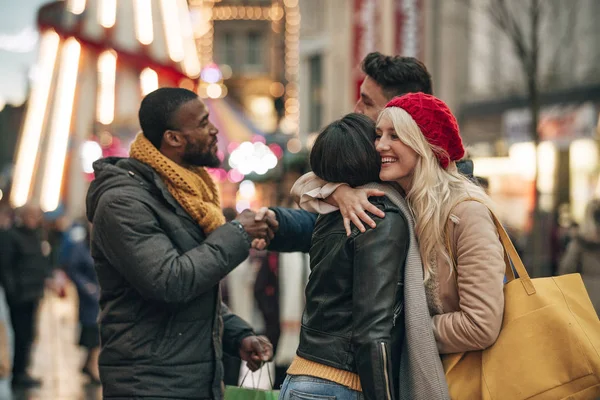 Side view of two couples saying goodbye to each other on the city street. The two men are shaking hands and the two women are hugging each other.