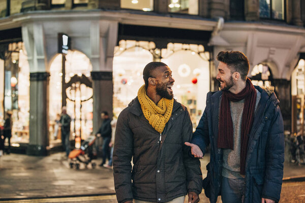 Front view of two men walking on a city street in the winter. Both men are wearing warm clothing, looking at each other and talking.