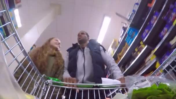 小さな女の子はスーパーで買い物食べ物を行う彼女の父を助けています リストを見ながら彼は台車を押しています — ストック動画