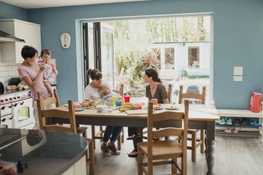 Üç yetişkin kadının evde mutfağa orta. İki kadın çocuklarını tutan ve atıştırmalık öğle yemeğinde. 