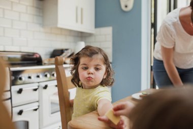 Bakış açısı küçük bir kız mutfak masasında yemek verildi. Küçük kız gıda üzerine odaklanmıştır ve ağzının kırıntıları vardır.