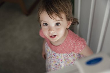 Yüksek açı bakış bir emniyet bebek Kapı öbür ucunda duran küçük bir kız. Küçük kız kameraya arsız ufak bir gülümseme ile yukarıya bakıyor.