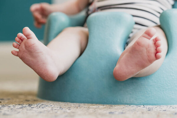 Low angle front view of a unrecognisable baby. The baby is sitting in a floor seat, the focus is on the babies feet.