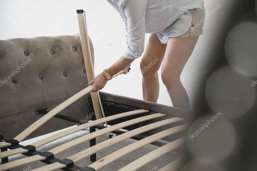 Mature woman is building her bed in her new home. She is placing wooden slats on the bed frame. 