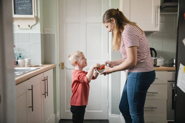小男孩和他的母亲站在 Kicthen 在房子里 小男孩妈妈正在拿着一碗草莓 而这个小孩拿一些零食 — 图库照片