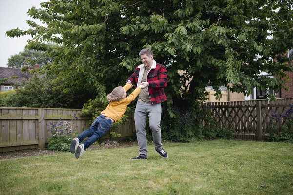 Мальчик веселится со своим отцом. Отец держит своих сыновей за руки и размахивает ими, смеясь и улыбаясь.
.