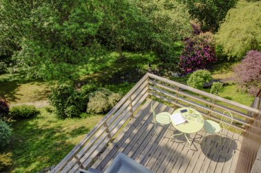 Yüksek bir görünüm hepsinde Ahşap balkon ormanlık bir alana bir parlak yaz gününde vurdu, yeşil bir masa ve sandalyeler balkon.