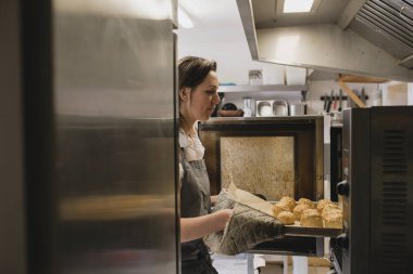 Orta yetişkin kadın baker pişmiş çörekler dışında fırın tepsisinin çıkarılması.