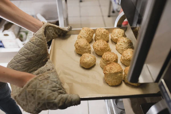 Unrecognisable person wearing oven gloves as they pull out a tray of scones from the oven.