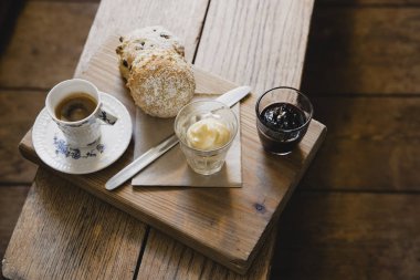 Yüksek açılı görünüş ahşap bir koltuk bir espresso kahve ve çörek. Bazı kaymak ve çörek için çilek reçeli.
