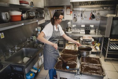 İş yerinde bir mutfakta ayakta Bayan baker. O bir tavada eritilmiş çikolata ve bir mutfak gereçler pour çikolata kullanarak.