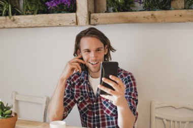 İçinde küçük bir kafe oturan orta yetişkin adam. O bir fincan kahve ile bir masada oturan ve telefonunu kullanarak bir selfie ele.