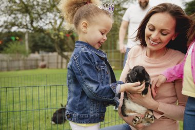 Küçük kız Paskalya partisinde evcil bir tavşanı okşarken heyecanlanıyor..
