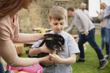 Dışarıda duran genç bir çocuk, orta yaşlı bir kadın ona tutması için bir tavşan uzatıyor.. 
