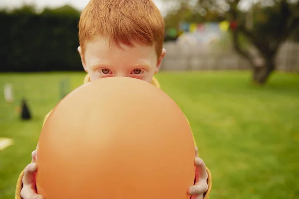Chlapec Přidržuje Oranžový Balón Před Obličejem Dívá Kamery Dívá Přes — Stock fotografie