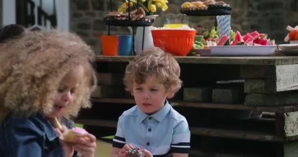 少年と彼の友人は 屋外ガーデン パーティーで座っています 彼はチョコレート ケーキを楽しんでいます — ストック動画