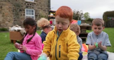 Heyecanlı küçük çocuk dışarıda oturmuş, arkadaşları etrafını sarmış. Elinde tuttuğu saksıdaki balçık onu hayrete düşürüyor.. 