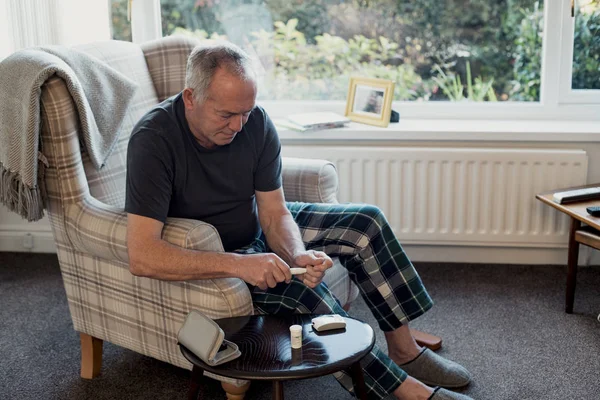 老年糖尿病患者正在他家客厅里检查自己的血糖水平 — 图库照片