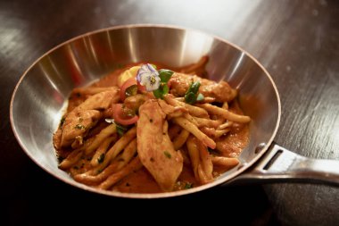 Gümüş bir tavada bir restoranda ahşap bir masa üzerinde sunulan Restoran tarzı arribiata pasta tavuk.
