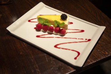 Tabakta bir dilim limonlu cheesecake. Böğürtlen ve ahududu ile süslenmiş..