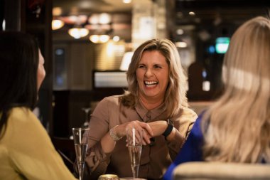 Olgun bir kadın gülüyor ve arkadaşları ile bir restoranda otururken gülümseyen omuz görünümü üzerinde.