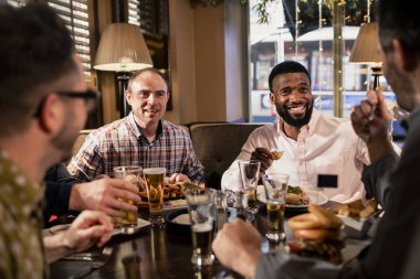 Small group of mid adult male friends enjoying some food in a restaurant. They are talking and enjoying each others company. clipart