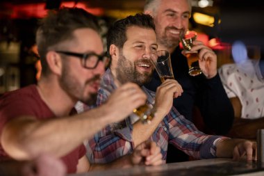 Three mid adult male friends enjoying a beer together in a bar.  clipart