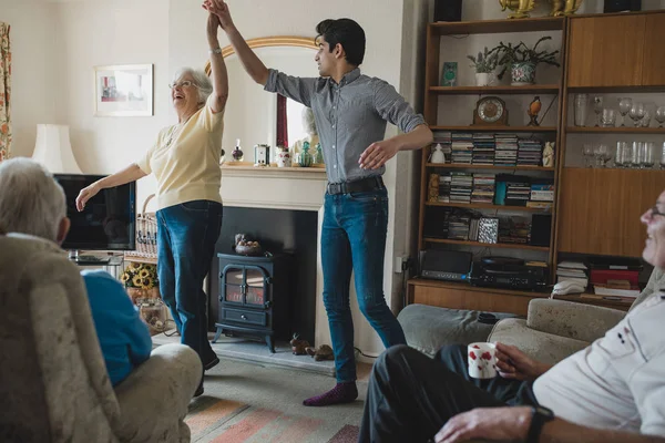 Senior woman is dancing in the living room with her teenage grandson.