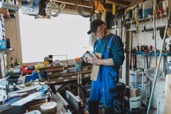 Senior man is working in his shed and is reading the label on a varnish.