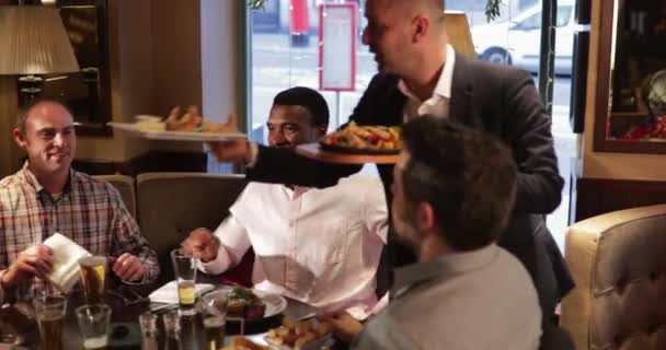 将一名男子服务员携带食物的镜头拍到一张男性朋友的桌子上 他们为食物的到来感到兴奋 — 图库视频影像