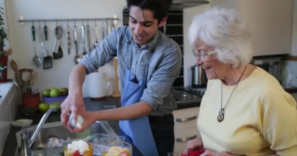 十代の少年は彼女の家の台所で彼の祖母と果物のコンポートを作る ボウルにクリームを入れてる — ストック動画