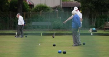 İki kıdemli yetişkinin çim bowlingi maçı izlerken yan görüntüsü. Birlikte duruyorlar..