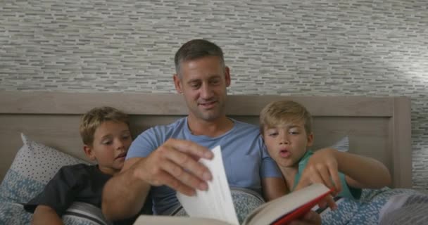 Yatakta Iki Küçük Oğluna Kitap Okuyan Bir Babanın Fotoğrafı — Stok video