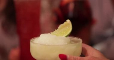 Tanınmayan bir barmen bir dilim limonla kokteyl hazırlıyor. Sonra da barda arkadaşlarıyla bekleyen bir kadına veriyorlar..