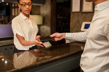 Otel resepsiyonisti, otele giriş yapan bir müşterinin bağlantısız ödemesini alıyor. Akıllı telefonuyla ödeme yapıyor..