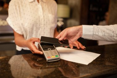 Otele giriş yapan bir müşterinin ulaşılamayan parasını alan tanınmamış bir bayan otel resepsiyonisti, parasını ödemek için akıllı telefonunu kullanıyor..