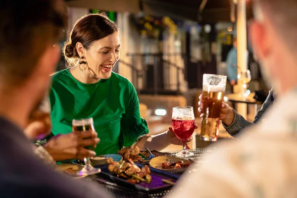 Friends drinking alcohol outdoors at a bar/restaurant, celebrating and having fun together.