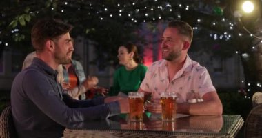 LGBTQI Çifti oturmuş dışarıda bir bar / restoranda şampanya içiyor, kutlama yapıyor ve birlikte eğleniyorlar..