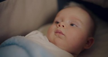 Küçük, biraz şaşırmış bir bebek bebek bebek arabasında yatıyor, nazikçe gülümsüyor..