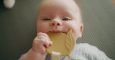 Oyun hasırının üzerinde uzanmış, ip çiğneyen sevimli bir bebek. Tatlı ve neşeli bir yüz ifadesini gösteren bebek yüzünün yakın çekimi.
