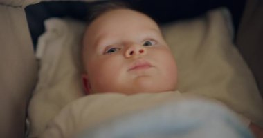 Bebek arabasında yatan gülümseyen bir çocuğun yakın çekimi. Neşeli ifadesini huzurlu bir ortamda yakalıyor..