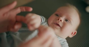 Sevimli bebek paspasın üzerine uzanmış annenin ellerini tutuyor, gülümsüyor ve dilini dışarı çıkarıyor, neşeli bağlılık anlarını paylaşıyor..