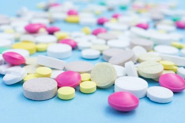 Çeşitli ilaç hapları, haplar ve kapsüller mavi arka planda.