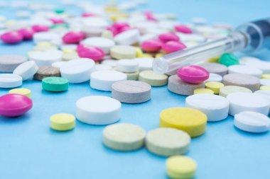 Çeşitli ilaç hapları, haplar ve kapsüller mavi arka planda.