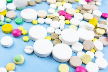 Çeşitli ilaç hapları, haplar ve kapsüller mavi arka planda.