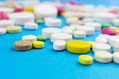 Çeşitli ilaç hapları, haplar ve kapsüller mavi arka planda.